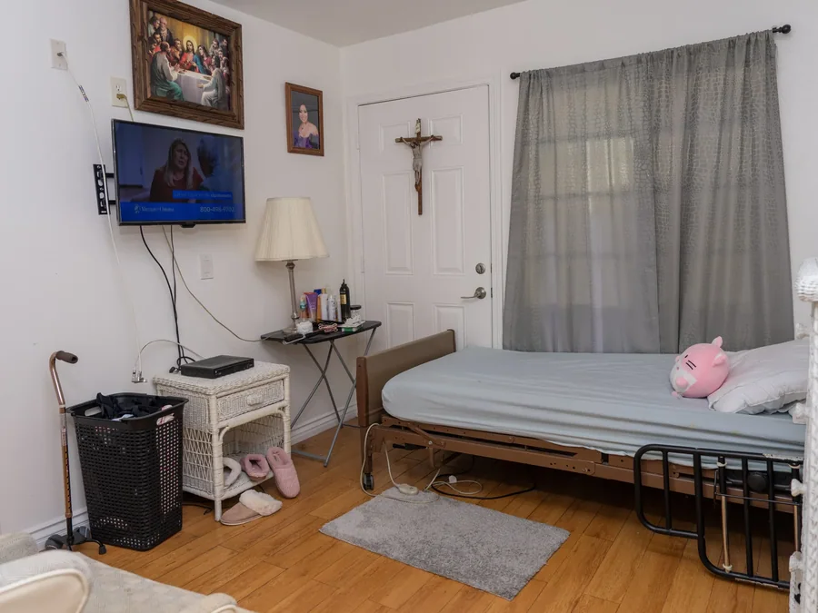 Private resident bedroom featuring adjustable hospital bed, television, personal belongings, and accessibility features