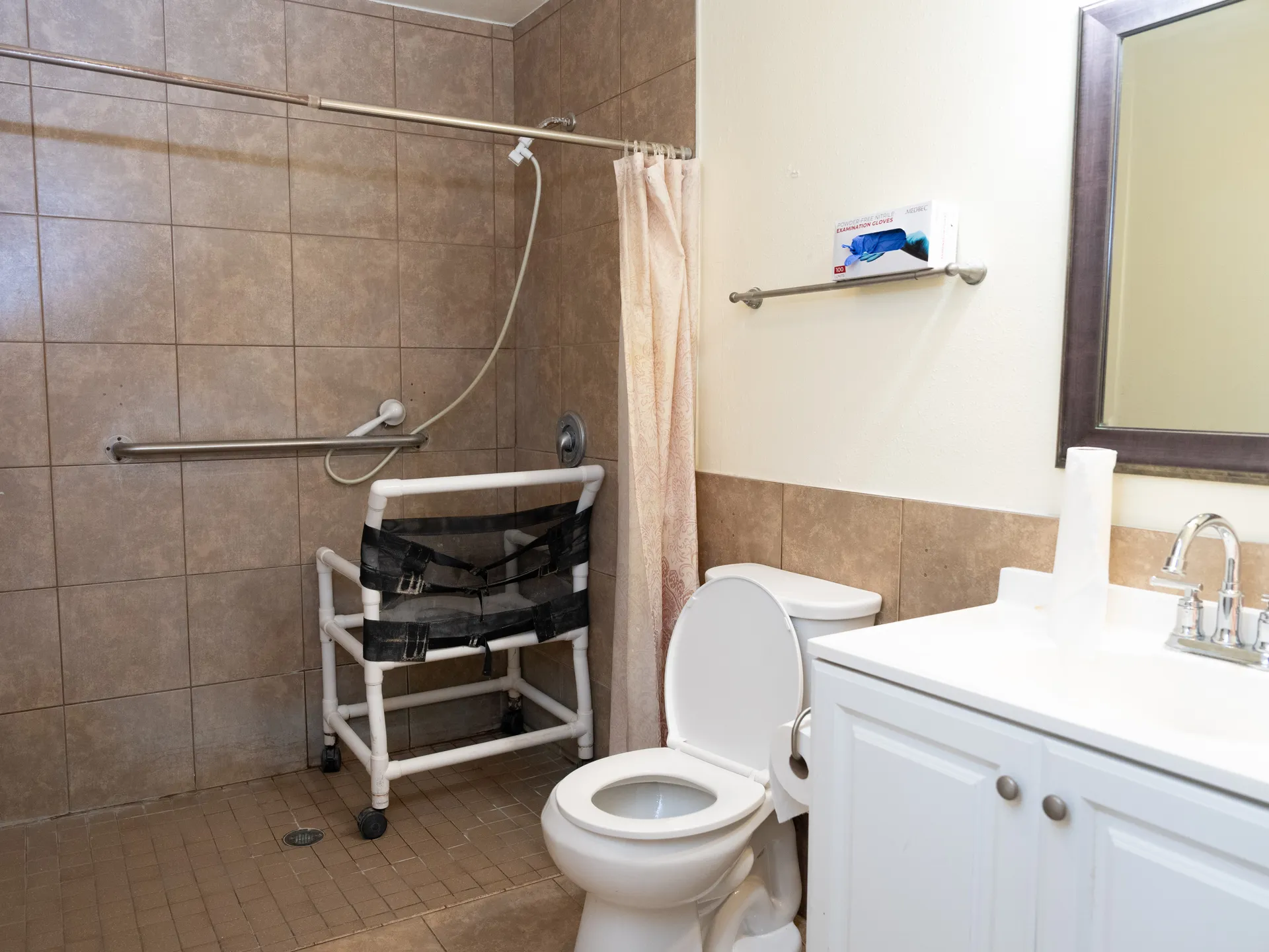 Accessible bathroom featuring roll-in shower with grab bars, mobile shower chair, and ADA-compliant fixtures