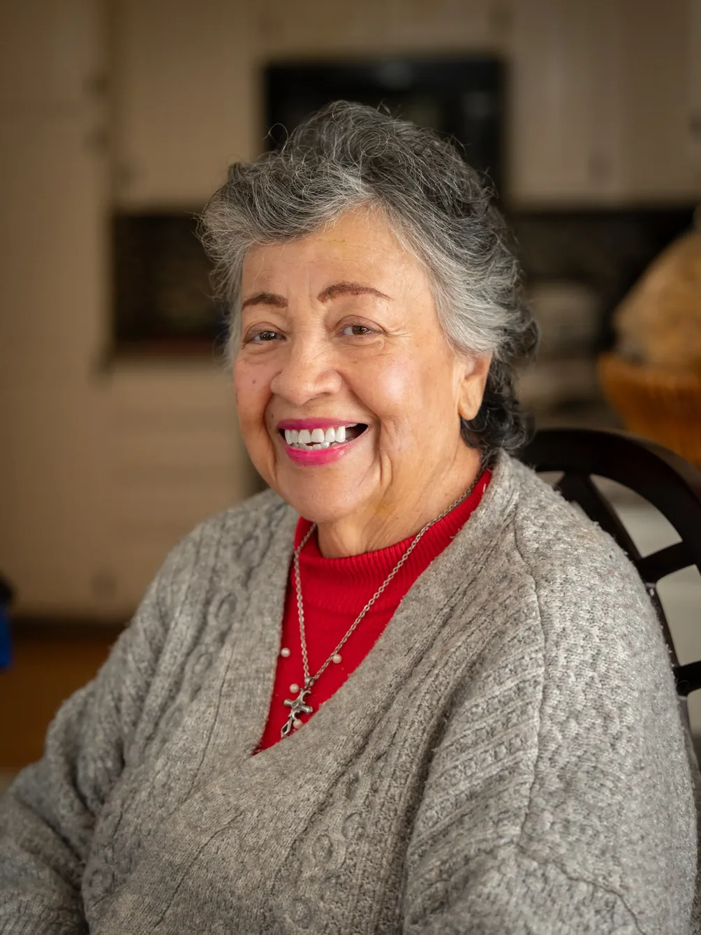 Smiling senior woman resident in comfortable home setting wearing gray cardigan and red shirt